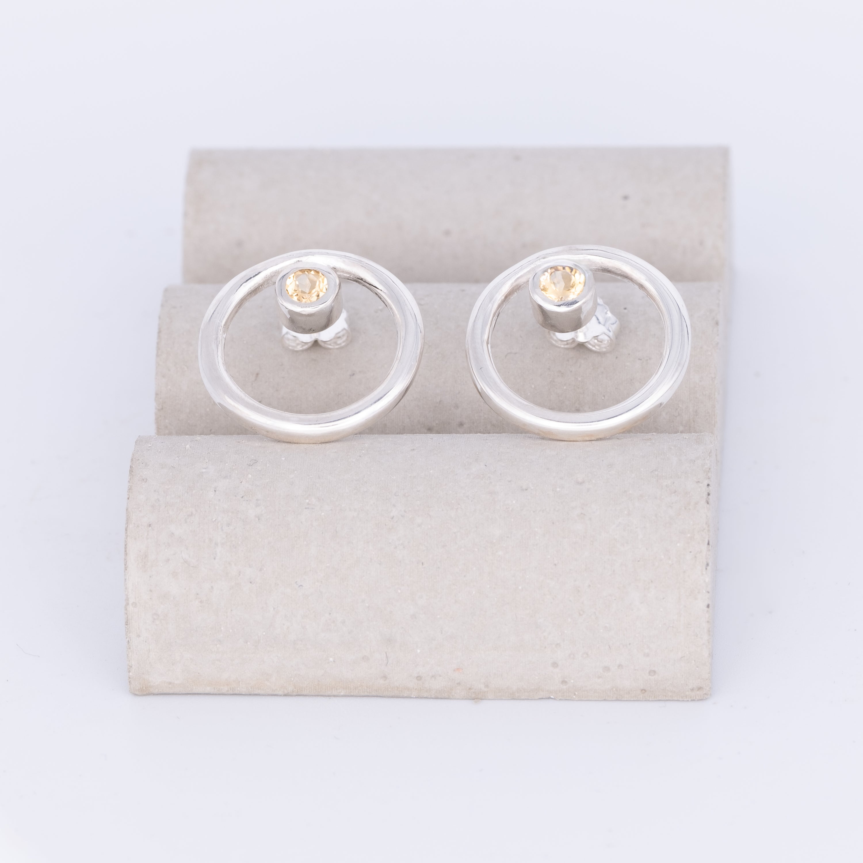 Silver earrings with clear gemstones on a beige card against a white background