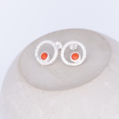 Silver earrings with orange stones on a white stone surface coral