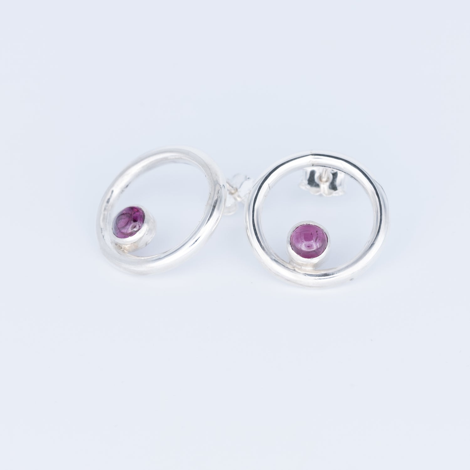 Silver earrings with purple gemstones on a light gray background