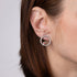 Close-up of an ear wearing a silver earring with a red gemstone on a neutral background