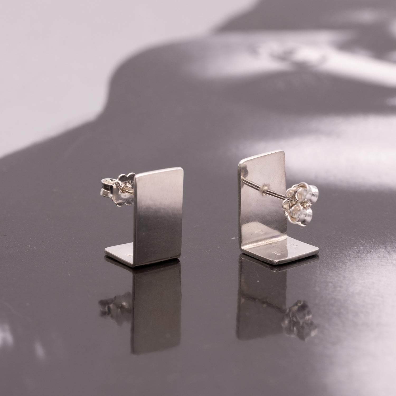Pair of silver earrings on a reflective surface