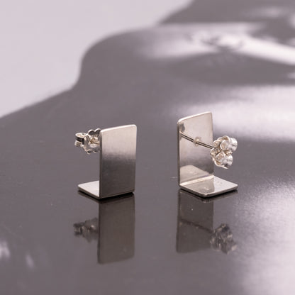 Pair of silver earrings on a reflective surface
