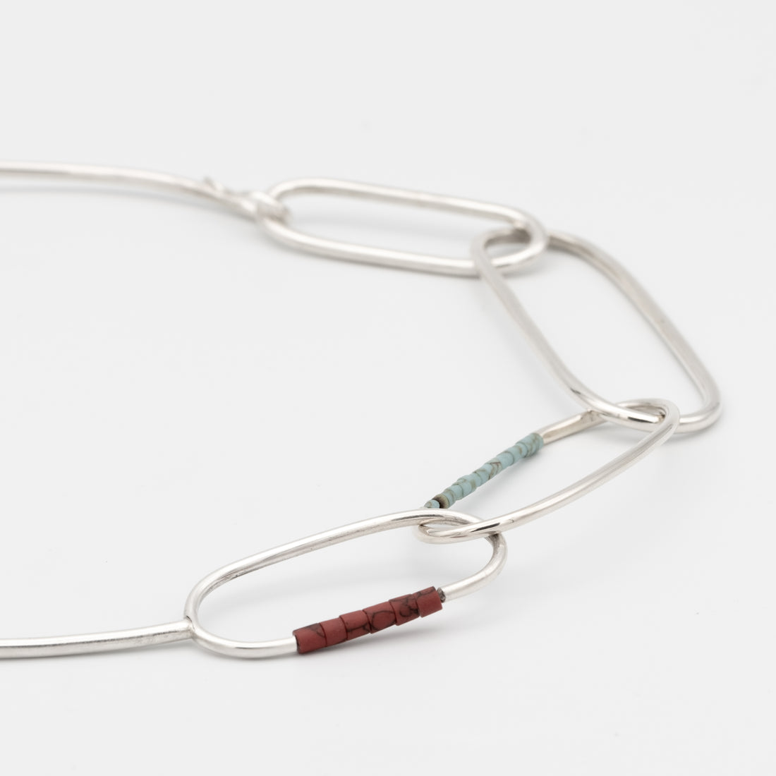 Silver necklace with a small brown bead on a white background