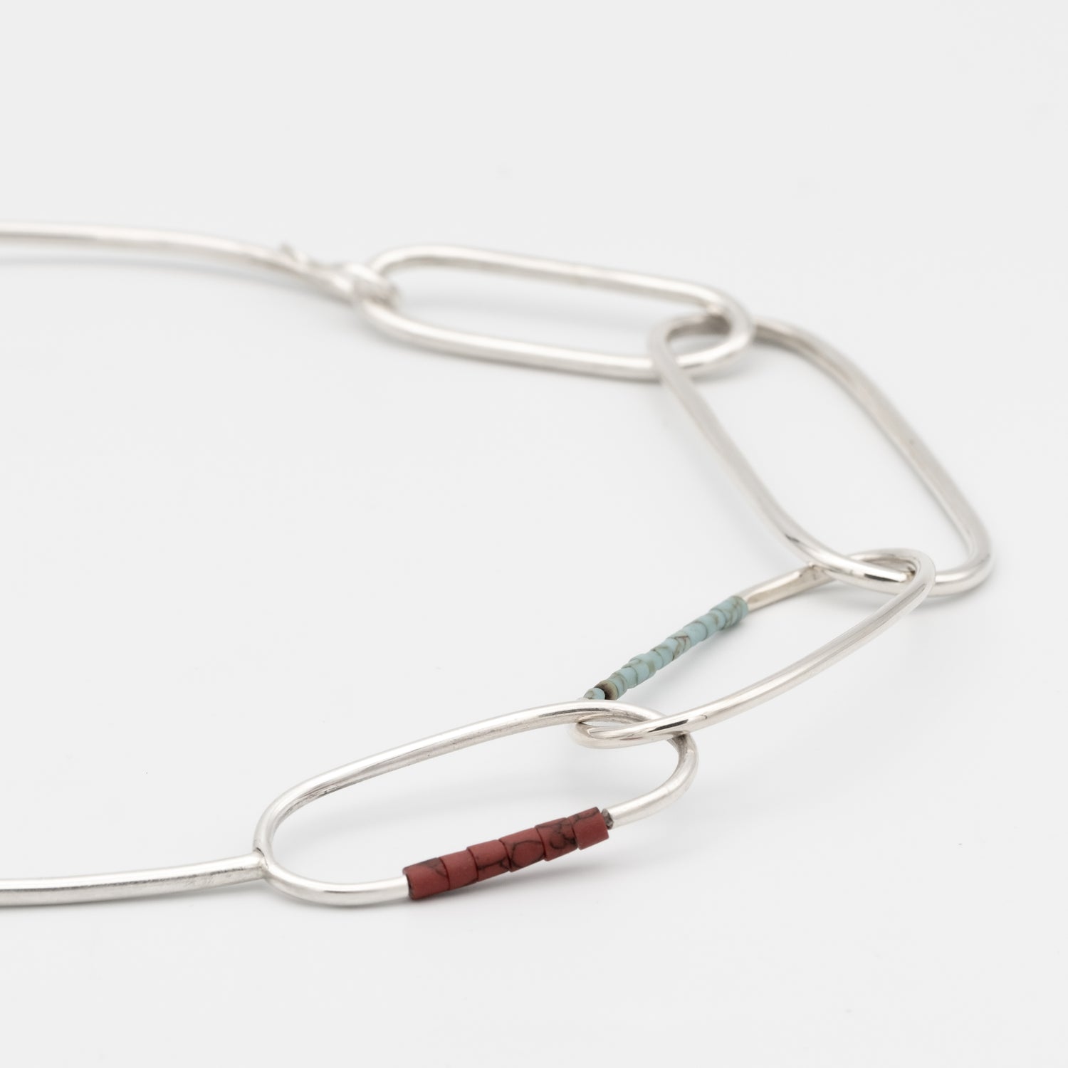 Silver necklace with a small brown bead on a white background