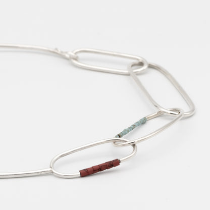 Silver necklace with a small brown bead on a white background