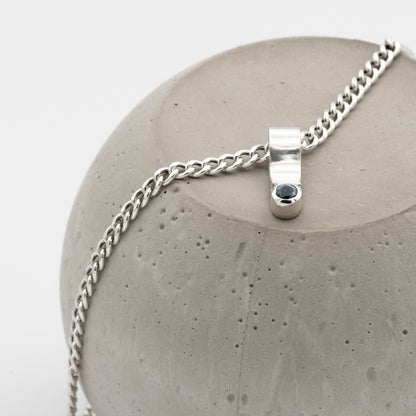 Silver necklace with a pendant on a concrete surface