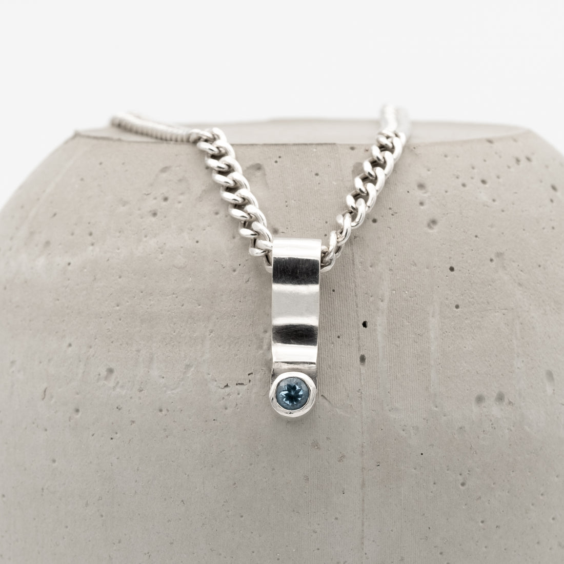 Silver necklace with a blue gemstone pendant on a textured gray surface