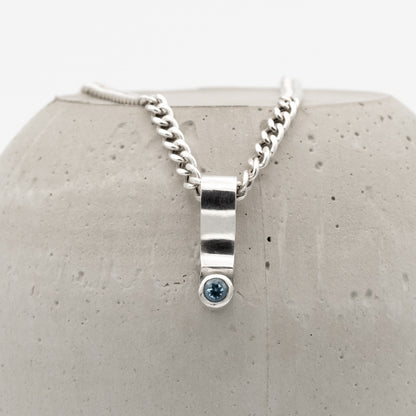 Silver necklace with a blue gemstone pendant on a textured gray surface