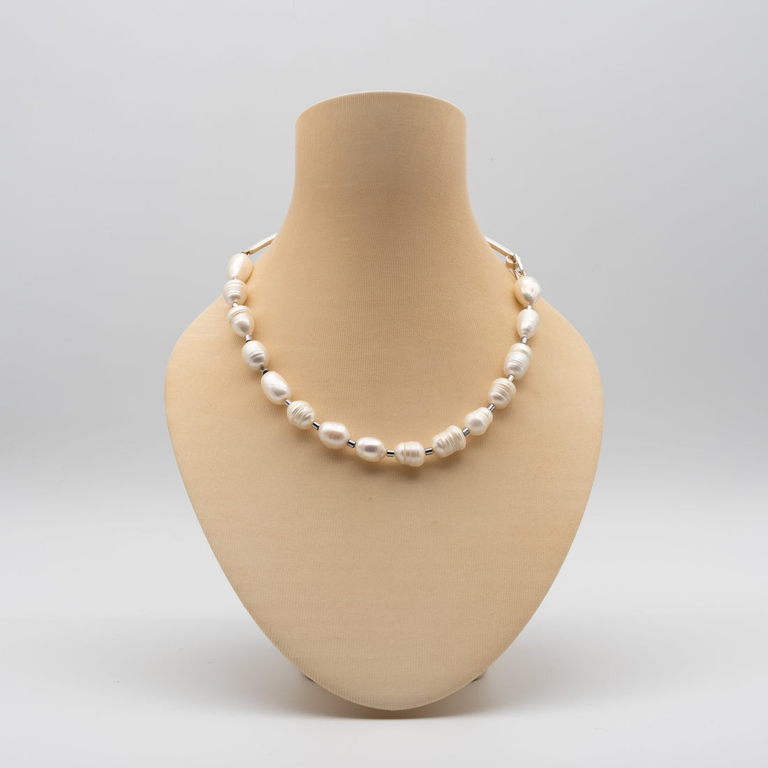 Pearl necklace on a beige mannequin bust against a light gray background