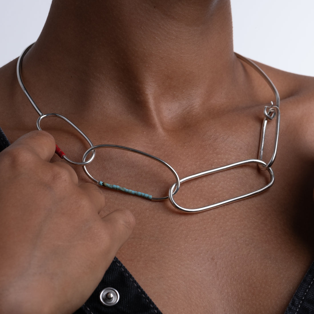 Person wearing a silver necklace with a close-up of the necklace on a neutral background