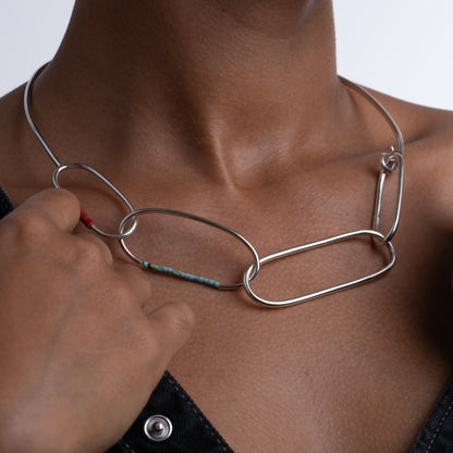 Person wearing a silver necklace with a close-up of the necklace on a neutral background