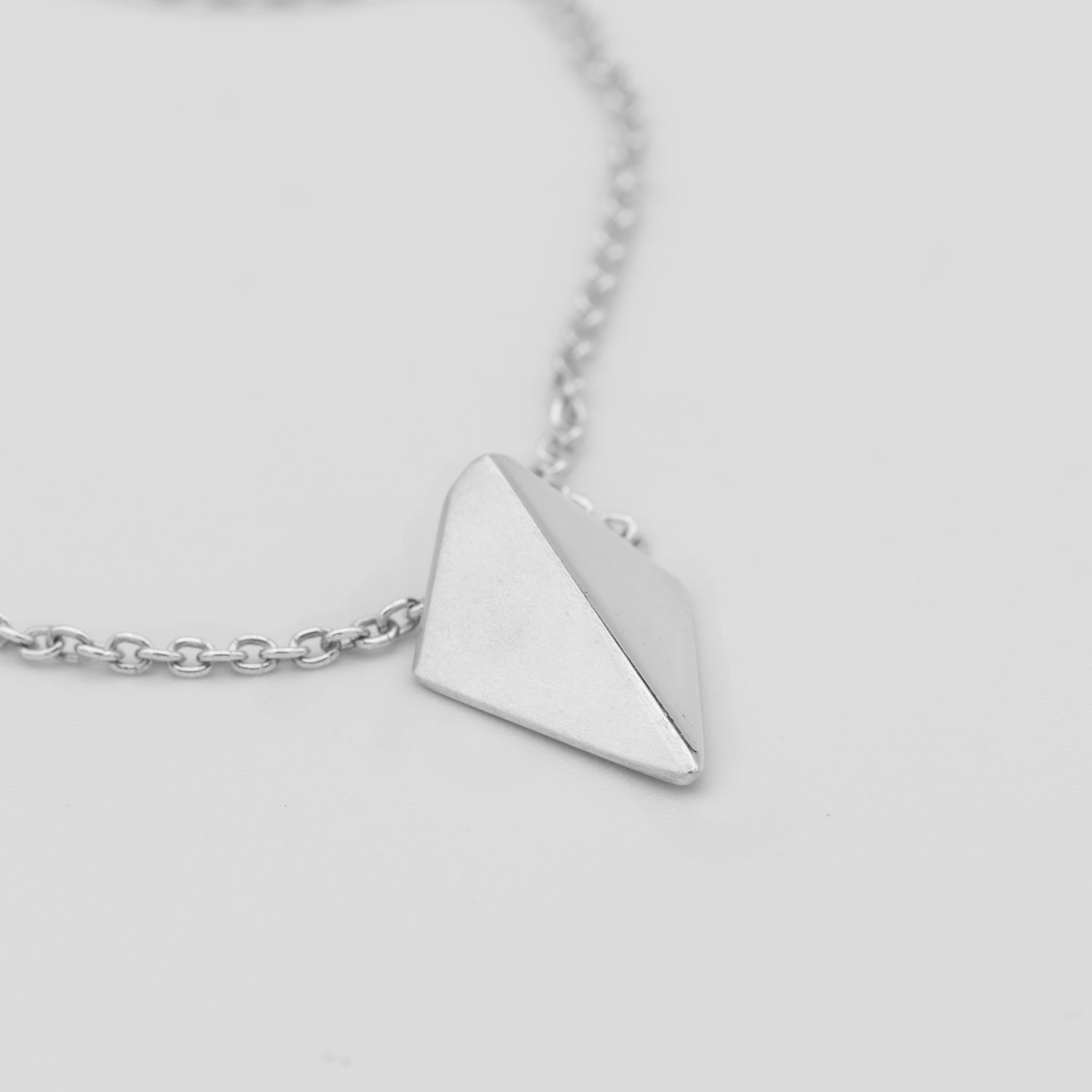 Silver necklace with a pyramid-shaped pendant on a light gray background