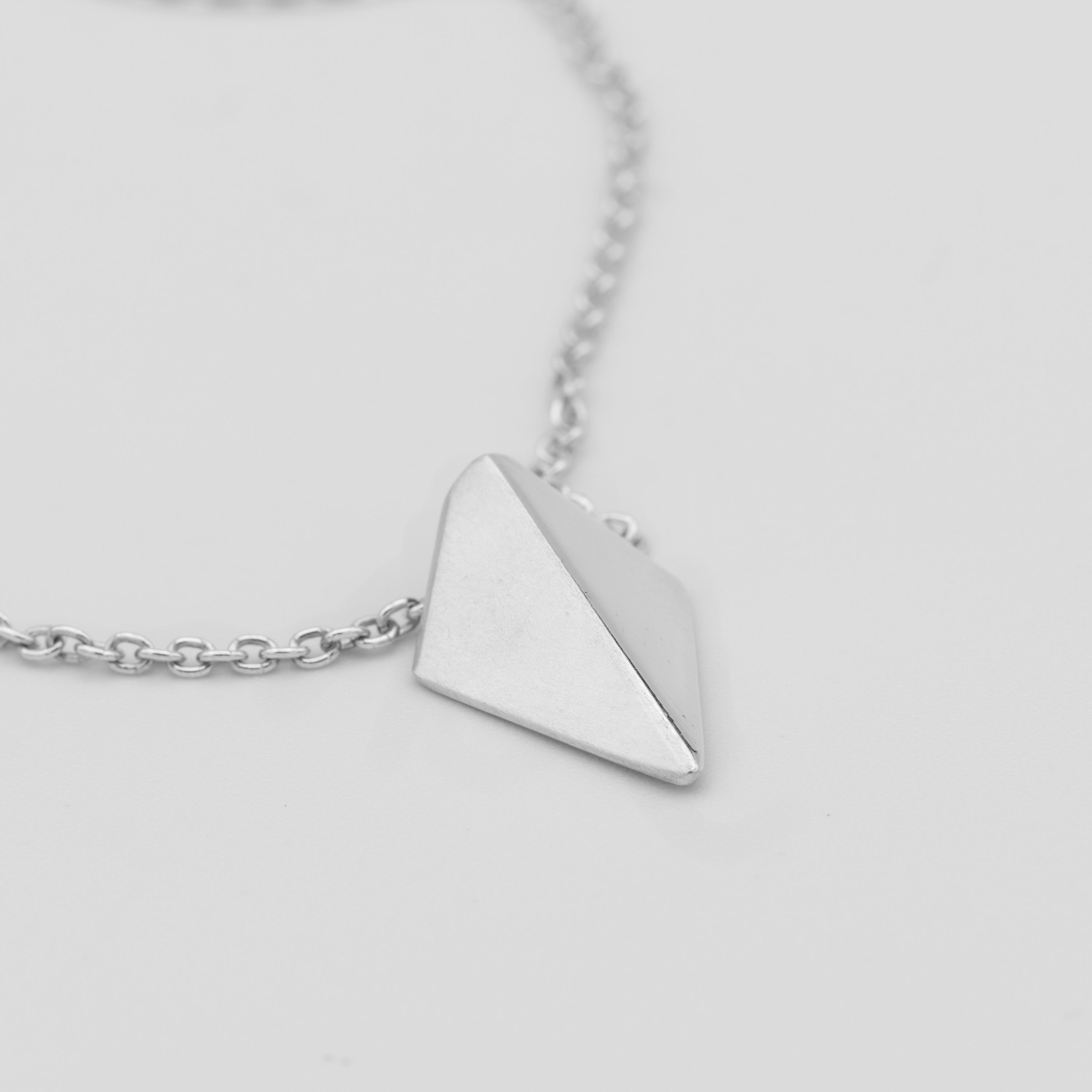 Silver necklace with a pyramid-shaped pendant on a light gray background