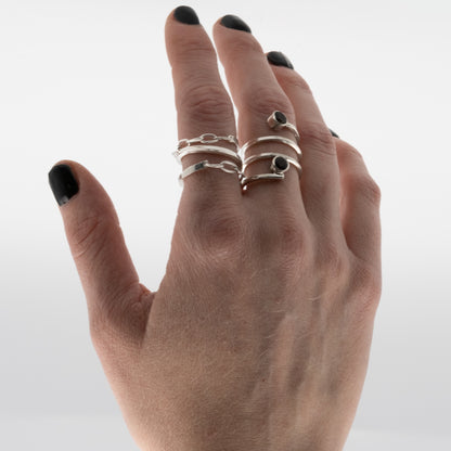 Hand wearing multiple silver rings with black gemstones on a white background