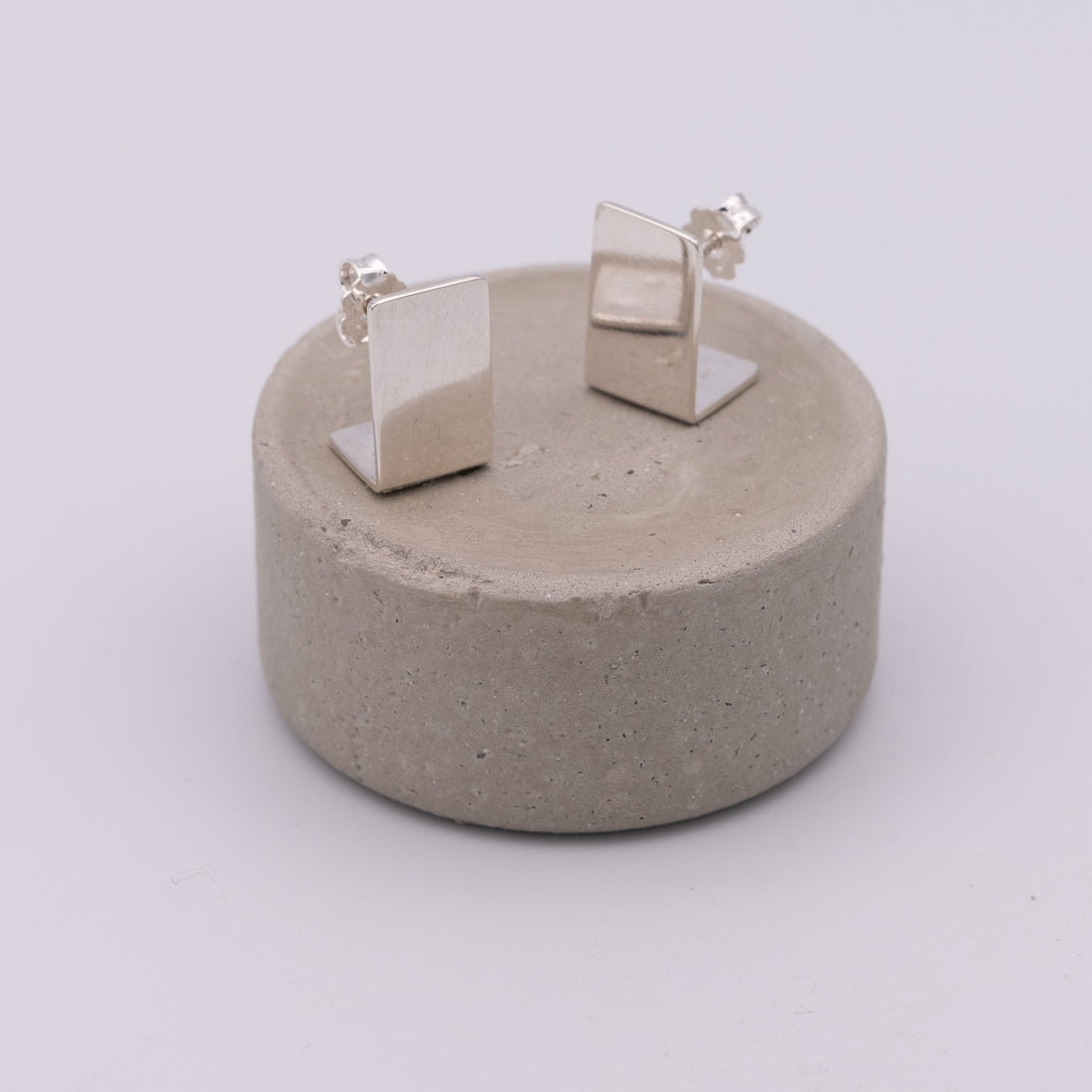 Pair of silver square earrings on a concrete stand against a white background