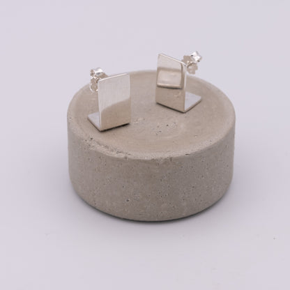 Pair of silver square earrings on a concrete stand against a white background