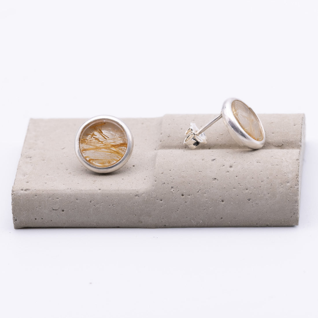 Silver earrings on a gray stone stand with a white background
