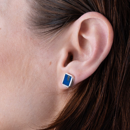 Close-up of an ear wearing a blue and silver earring. lapis lazuli