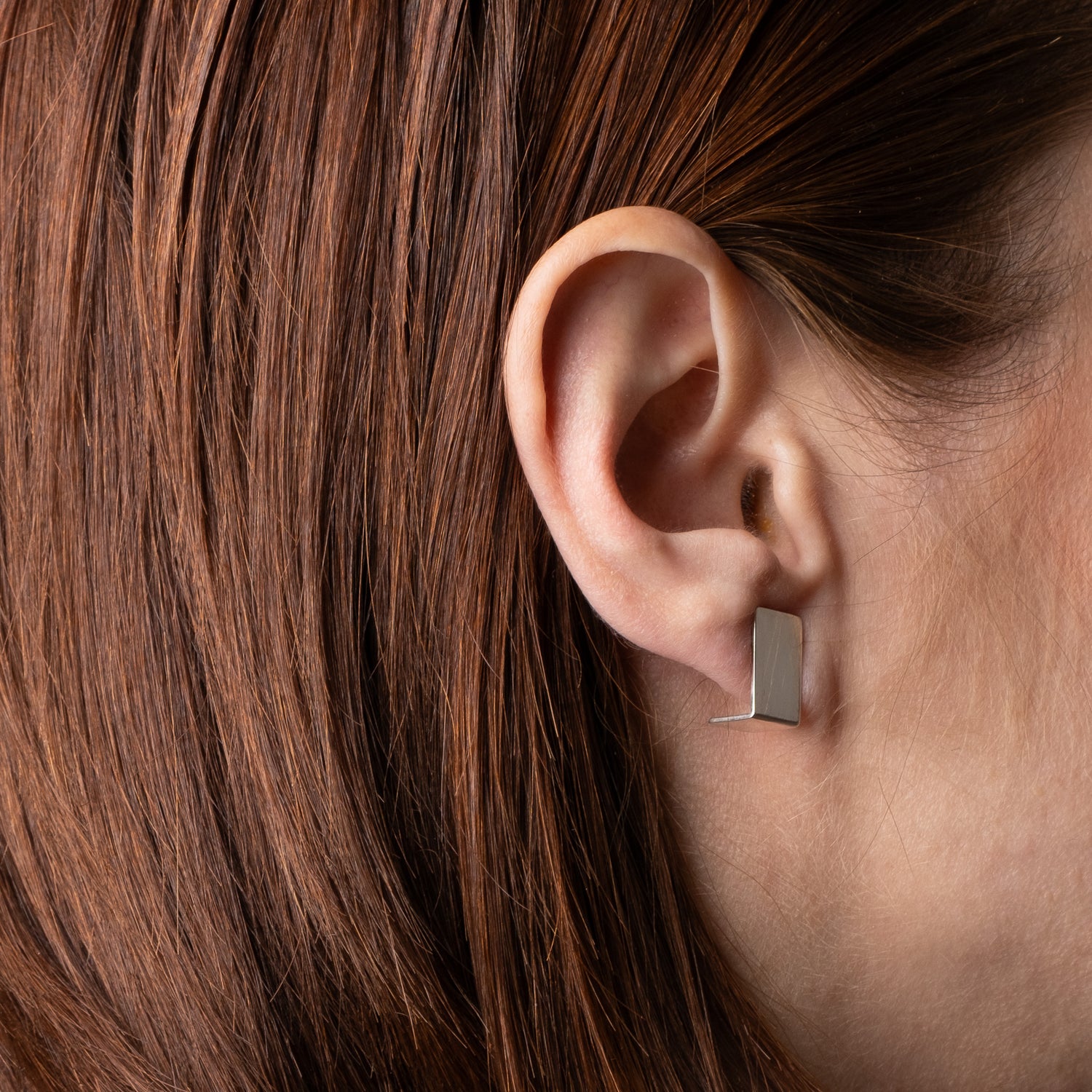 Close-up of an ear wearing a square earring with brown hair.