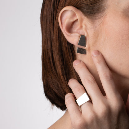 Person wearing a geometric earring and ring on a plain background