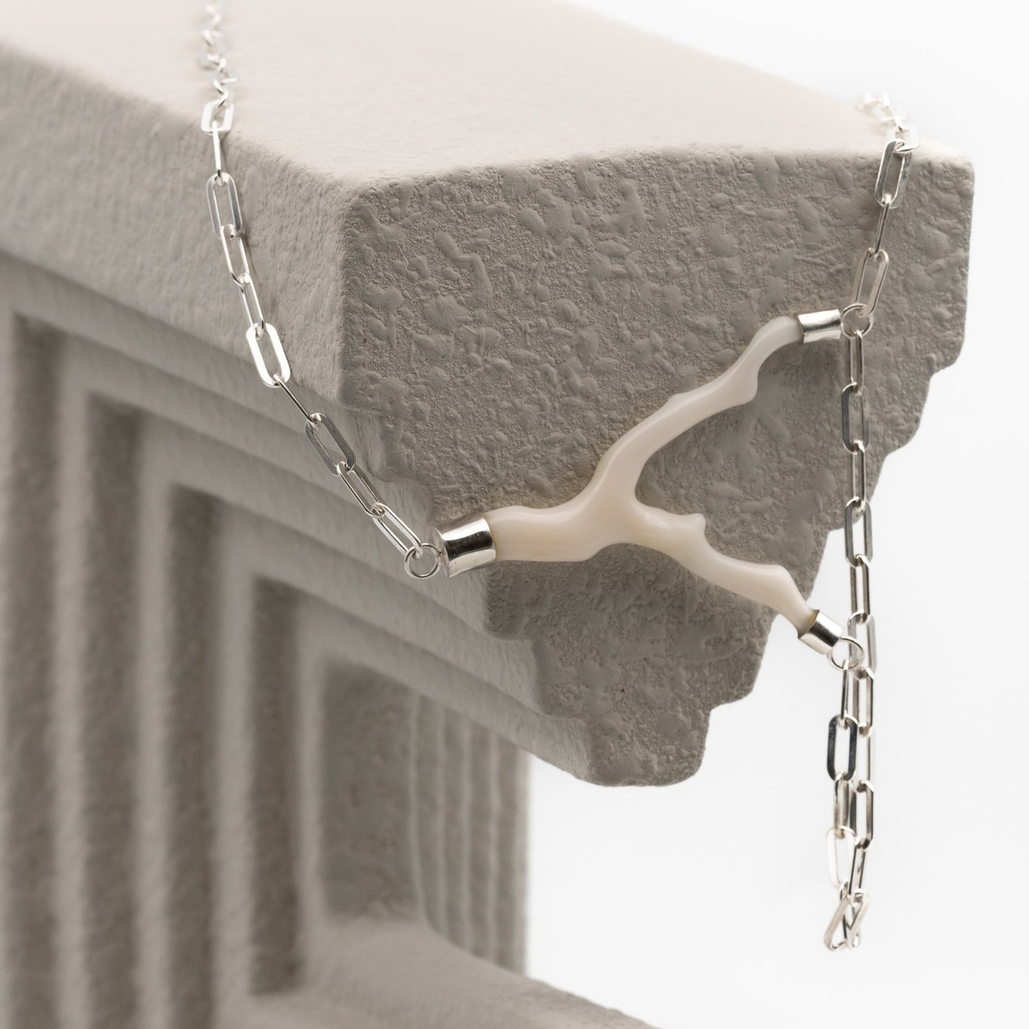 A close-up of a silver chain necklace with a unique branch-shaped white coral  draped over a textured gray stone ledge.