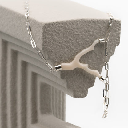 A close-up of a silver chain necklace with a unique branch-shaped white coral  draped over a textured gray stone ledge.