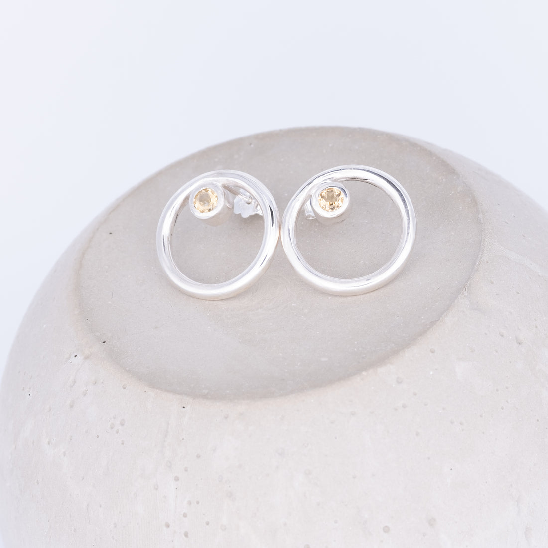 Silver earrings with small round stones on a light gray stone surface