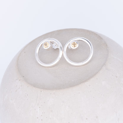 Silver earrings with small round stones on a light gray stone surface